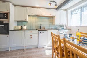 a kitchen with white cabinets and a table with chairs at Polrunny Farm Blackberry Cottage - Cornwall bliss in sight of the sea in Boscastle +28 photos