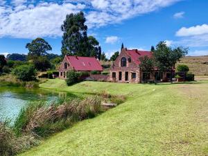 an old house with a red roof next to a river at Millstream Farm Cottages in Dullstroom