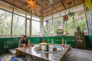 a person sitting at a table in a room with windows at Pahadirovers Homestay & Cafe in Kasol