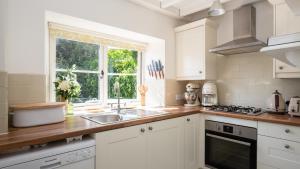 a white kitchen with a sink and a window at Honeywick Cottage in Stow on the Wold