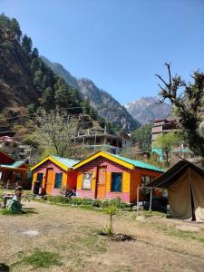 Un grupo de casas coloridas con montañas al fondo. en Parvati Hill Cottage By Soma Stays, en Kasol