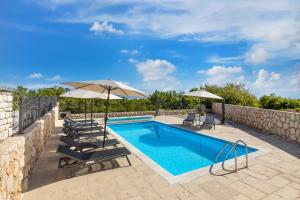 una piscina con sillas y sombrillas junto a una pared en Villa Maja, en Vrbnik