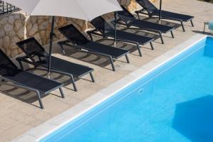 Una fila de sillas con sombrillas junto a una piscina. en Villa Maja, en Vrbnik 41 fotos más