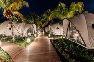 a wooden walkway leading to luxury tents with palm trees at Cocoon Resort Kuching in Kuching