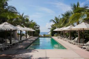 a swimming pool with chairs and umbrellas and the ocean at El Origen Villas & Spa-Puerto Escondido in Puerto Escondido