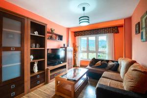 a living room with orange walls and a couch and a tv at Durmiendo en el Paraiso in Llanes