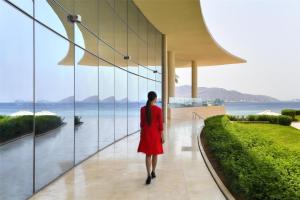 Una mujer con un vestido rojo caminando por un pasillo mirando el agua en Kempinski Hotel Aqaba, en Áqaba