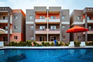 a swimming pool with an umbrella and chairs and a building at Villaggio lavie in Ras Sedr