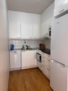a white kitchen with white appliances and wooden floors at Warm and cozy one-bedroom & Sauna in Vantaa