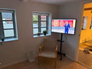 a room with a tv on a wall with a chair at Rolighed B&B in Hinnerup