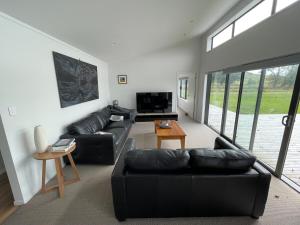 a living room with a black leather couch and a television at Clifton Bay Cottage in Te Awanga