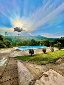 a large swimming pool with the sun in the background at Recanto dos Loureiros - Serrinha do Mendanha in Marapicu