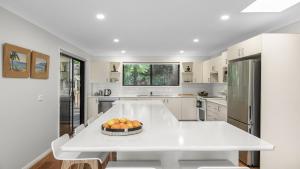 a white kitchen with a table with fruit on it at 'Bay Dreams at Killcare' by HolidayCo in Killcare