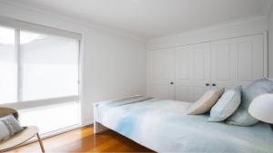 a white bedroom with a bed with blue pillows at 'Bay Dreams at Killcare' by HolidayCo in Killcare