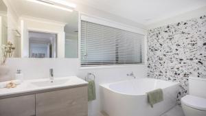 a white bathroom with a tub and a toilet at 'Bay Dreams at Killcare' by HolidayCo in Killcare +10 photos