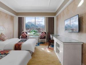 ein Hotelzimmer mit zwei Betten, einem Schreibtisch und einem Fenster in der Unterkunft Shangri-La Jilaideng Gucheng Hotel in Shangri-La