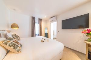 a white bedroom with a large bed and a flat screen tv at Les Capucines Saint Tropez in Saint-Tropez