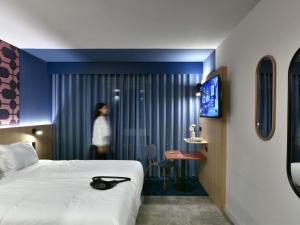 um quarto de hotel com uma cama e uma mulher em pé no chuveiro em Ibis Styles Charleroi Airport Aero 44 em Charleroi mais 37 fotografias
