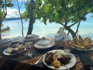 a table with plates of food on a table with the ocean at Intum Homestay in Kri