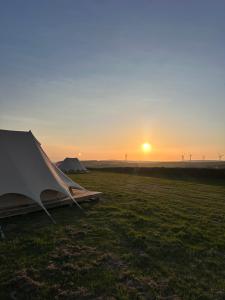 a tent in a field with the sunset in the background at Springfield glamping in Marwood +3 photos