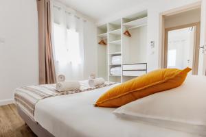 a white bedroom with a large bed with an orange pillow at Casamea - T3 U Benestà in Talasani