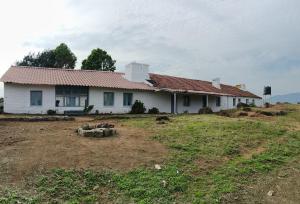 una casa bianca con un tetto rosso su un campo di Cascade Meadows Bungalow with Waterfall View a Kotagiri