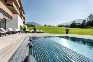 a swimming pool next to a building with chairs at Klosterhof – Alpine Hideaway & Spa in Bad Reichenhall