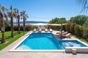 a pool with chairs and umbrellas in a yard at Seaview Villa Stanka with Pool and attached Jacuzzi in Kaštela