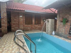 a swimming pool in front of a brick house with a water fountain at Lelangit Inn in Port Dickson