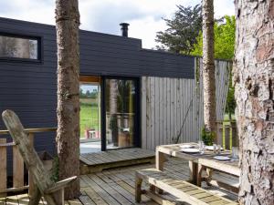 a black cottage with a wooden deck and a table at La Cafoutche Tiny - 5 personnes in Gommenecʼh