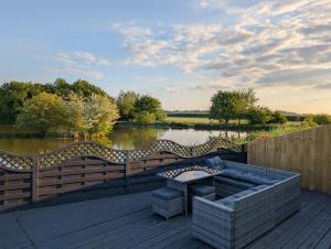 a patio with a couch on a wooden deck next to a lake at Aylesbury Lodge in Shepton Mallet