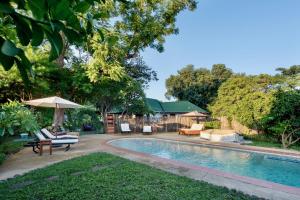 a swimming pool with chairs and an umbrella in a yard at Kamunjila Lodge in Livingstone
