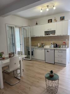 a kitchen with white cabinets and a desk and a table at Apartman Iskra in Bijela