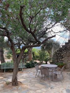 a table and chairs under a tree next to a stone wall at Les Meublés de la Corniche in Argelès-sur-Mer