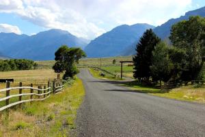 a road with a fence and mountains in the background at Family Cabin Rental on Beautiful Ranch near Yellowstone National Park, Wyoming in Wapiti