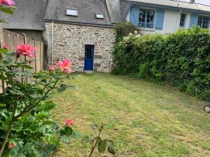 a yard with a house with a blue door and pink flowers at Petite Maison de Pêcheur in Mesquer