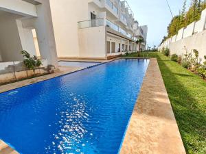 a blue swimming pool in front of a building at Appart Moderne Vue mer latérale & piscine - Plage des Sablettes El Mansouria in Ben Slimane