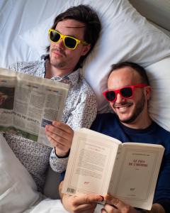 two men wearing sunglasses laying in bed reading books at Hôtel Couvent du Franciscain Centre ville in Strasbourg