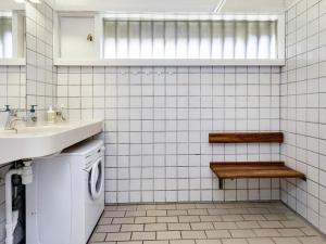 a white tiled bathroom with a sink and a washing machine at Holiday home Karrebæksminde XII in Karrebæksminde +61 photos