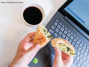 a person holding a sandwich in front of a laptop at B2 Hat Yai Rat Uthit Boutique & Budget Hotel in Sathani Hat Yai