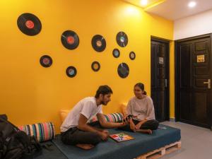 two people sitting on a bed in a room with clocks on the wall at The Hosteller Fort Kochi in Cochin