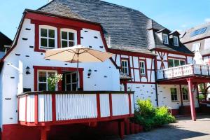 Una casa blanca y roja con un paraguas al frente. en Altes Fährhaus Anno 1 6 3 3 Traumferienwohnung In Exponierter Moselufer Lage, en Traben-Trarbach