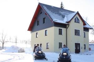 two people riding on snowmobiles in front of a house at Fewo Erzgebirge in Dorfchemnitz