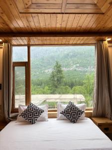 a bed with pillows in front of a large window at deja view orchard, old manali in Manāli