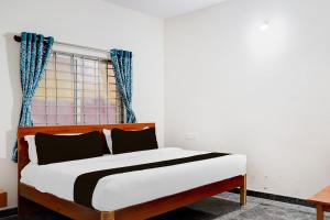 a bedroom with a bed and a window with blue curtains at Hotel O Sri Krishna Comforts in Bengaluru