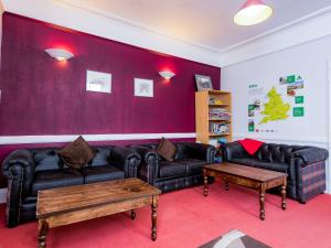 a living room with black leather couches and a red wall at YHA Coniston Coppermines in Coniston
