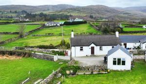 une maison blanche dans un champ avec des montagnes en arrière-plan dans l'établissement Carol Cottage, à Kilkeel