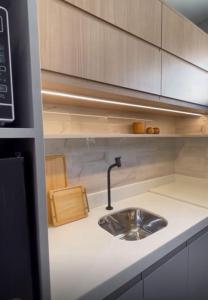 a kitchen counter with a sink and wooden cabinets at Apartamento moderno com 2 quartos e cama queen-size in Caruaru