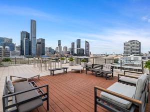 Un patio con bancos y mesas en un tejado con vistas al horizonte de la ciudad. en Stylish Apartment with Rooftop BBQ & Spa Access, en Brisbane