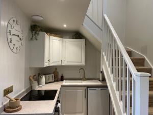 a kitchen with white cabinets and a clock on the wall at Wisteria Cottage - 2 bed near Bath & many NT sites in Holt